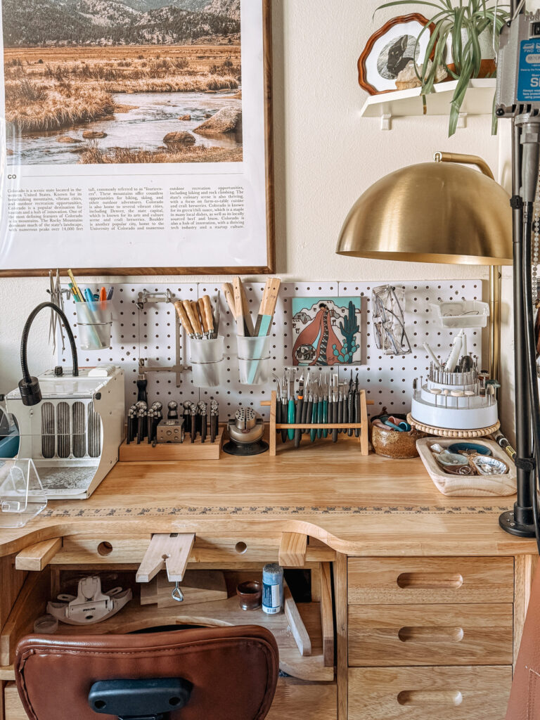 The Foreverie jewelry workbench with tools, artwork, and a golden lamp.