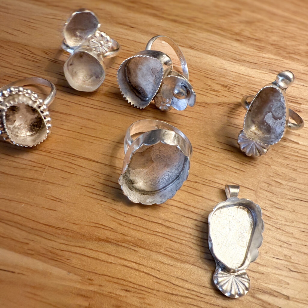 A collection of handcrafted sterling silver ring settings on a wooden workbench.