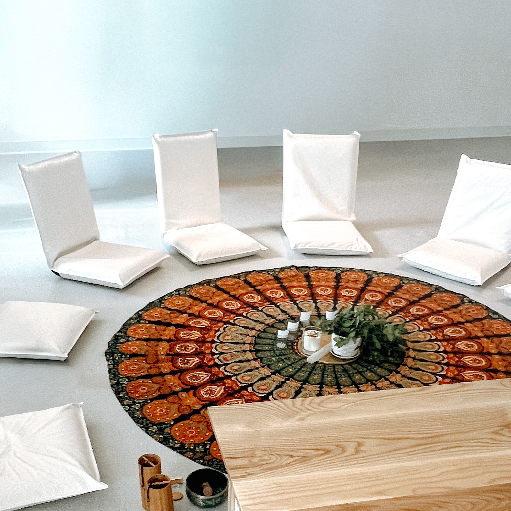 Minimal sound bath meditation circle with floor cushions, mandala rug, candles, and natural light