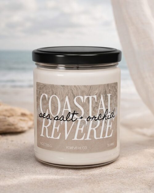 Coastal Reverie soy candle by Foreverie styled on sand with soft linen drapery and ocean in the background, sea salt and orchid scent.