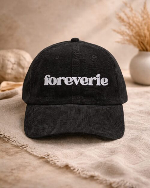 Black corduroy baseball cap with “foreverie” embroidered in white, styled on neutral linen background