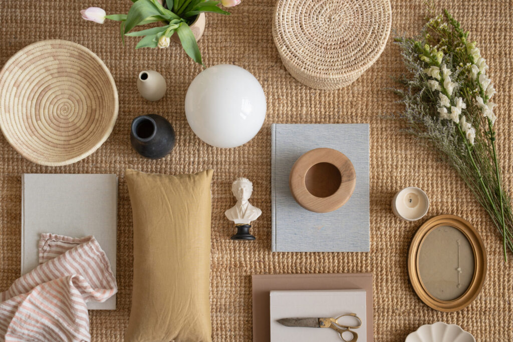 Flat lay of curated home and lifestyle objects including books, ceramic vessels, woven baskets, candle, flowers, and textiles