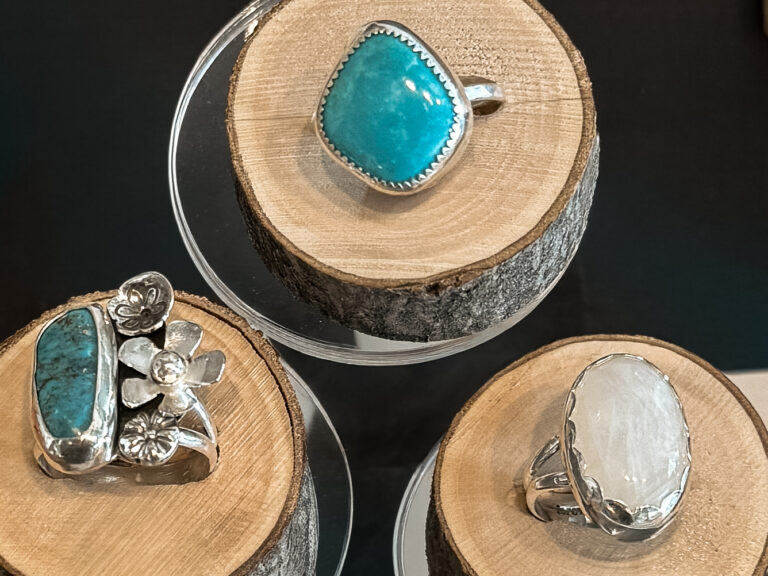 Handmade sterling silver turquoise and moonstone rings displayed on natural wood pedestals