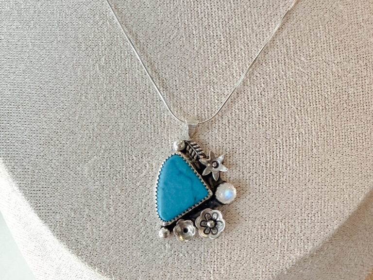 Handmade sterling silver turquoise pendant necklace with floral details on neutral linen bust