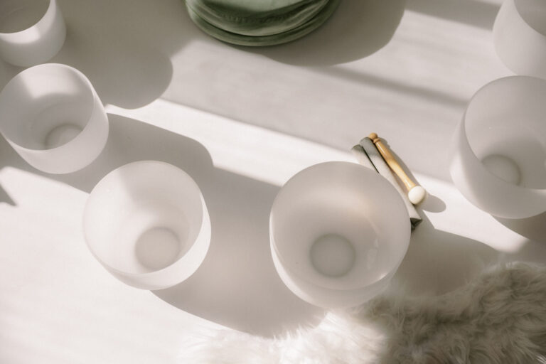 Frosted crystal singing bowls arranged with mallets on a white surface in soft sunlight.