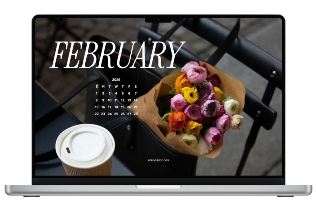 Laptop mockup displaying February 2026 desktop wallpaper with coffee cup and colorful flower bouquet on a café chair.