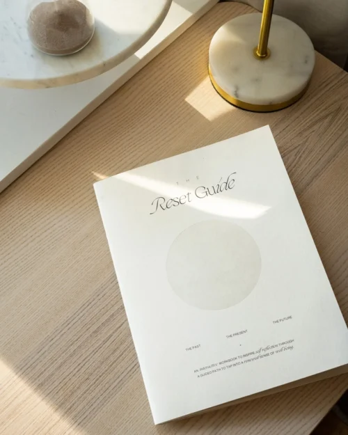 The Reset Guide workbook styled on a wooden table with soft natural light and minimal decor.