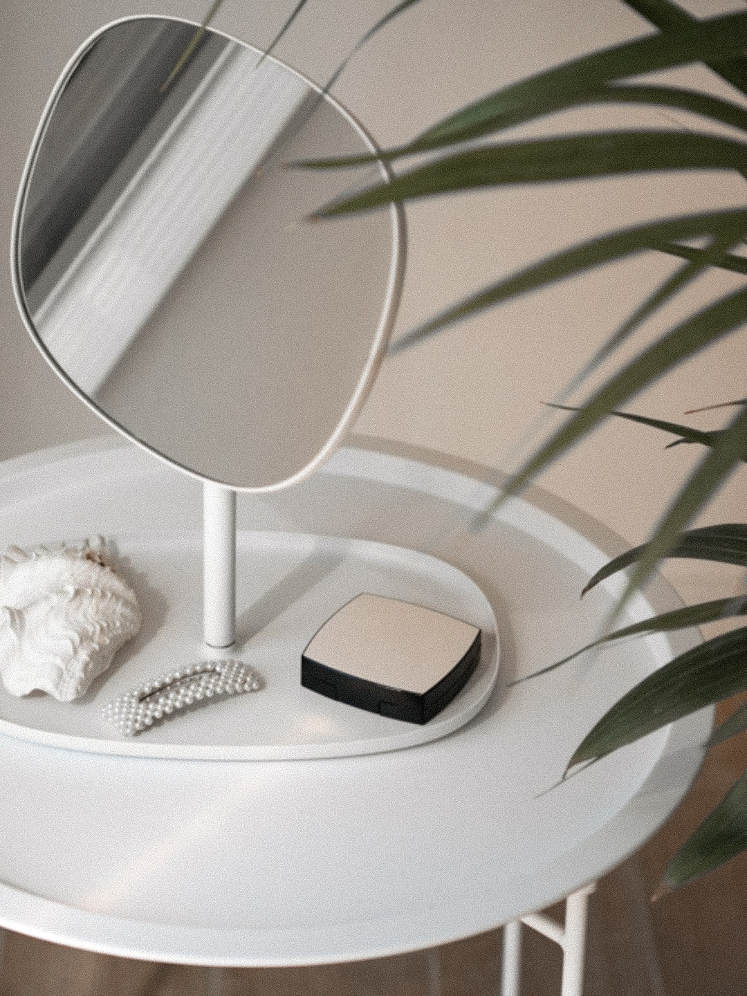 minimal white vanity tray with round mirror, seashell, pearl hair clip, and compact makeup on a soft neutral table