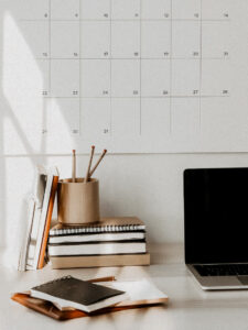 minimal desk with wall calendar, stacked notebooks, pencils in a cup, and laptop in soft natural lighting