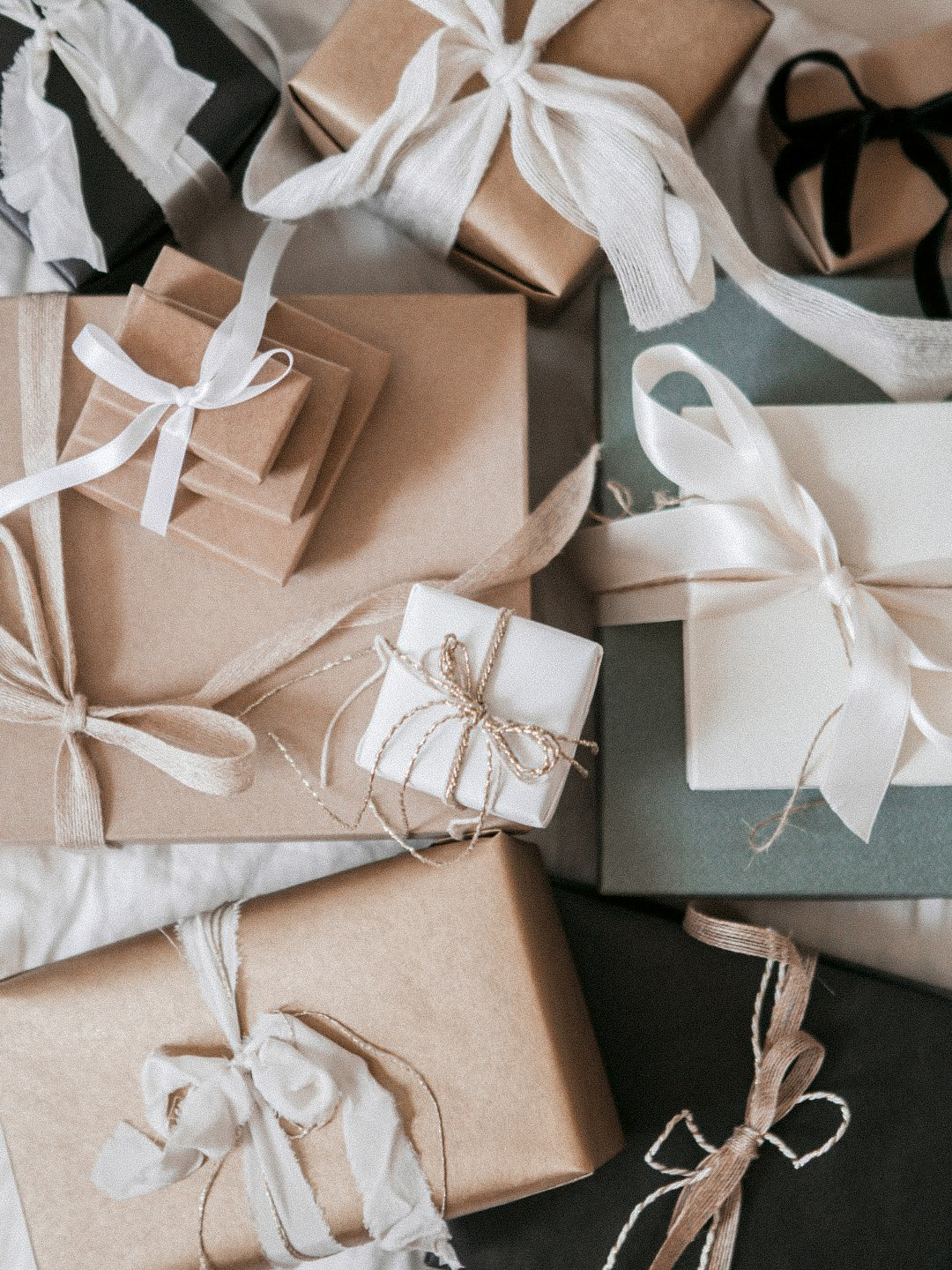 assortment of wrapped gifts in kraft paper and soft neutral tones tied with ribbon and twine