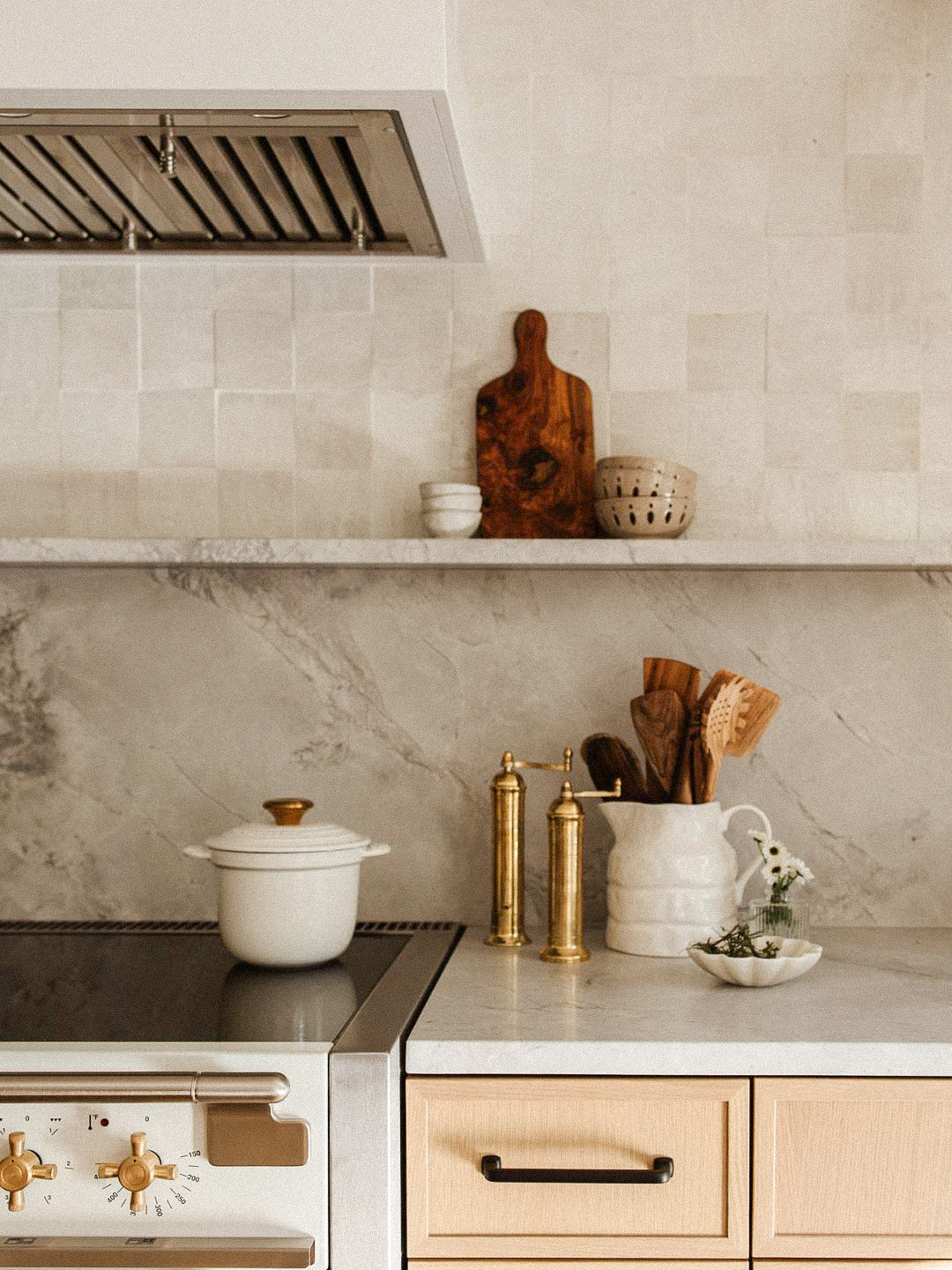 minimal kitchen with marble backsplash, wooden utensils, ceramic pitcher, and neutral cookware