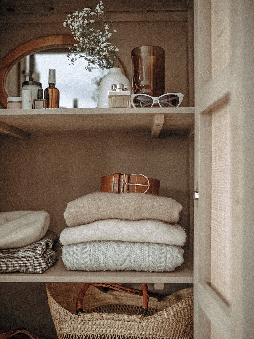 neutral wardrobe shelf with folded sweaters, leather belt, woven bag, and curated accessories