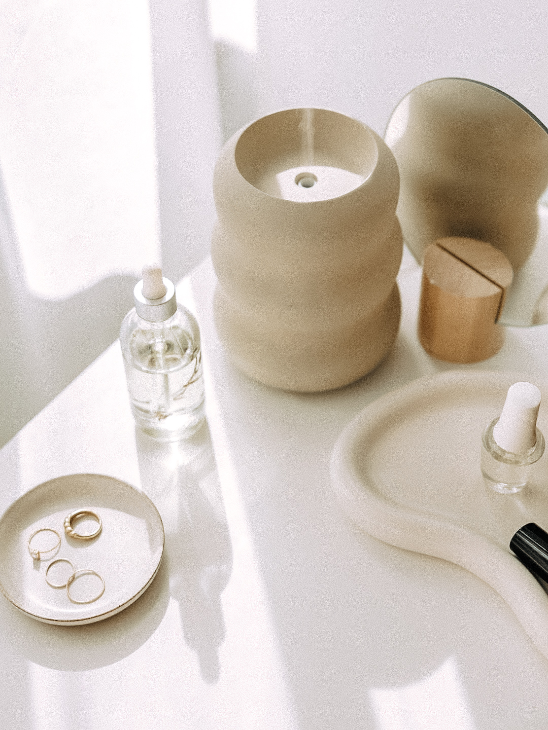 soft neutral skincare setup with glass serum bottle, ceramic tray, rings, and minimal beauty products
