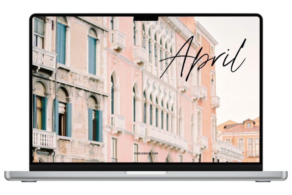 Laptop mockup displaying April 2026 desktop wallpaper with soft European buildings and pastel tones