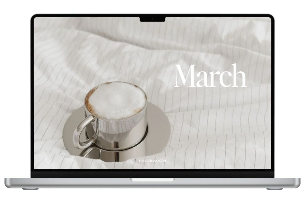 Laptop mockup displaying March 2026 desktop wallpaper with coffee on white bedding and soft neutral tones