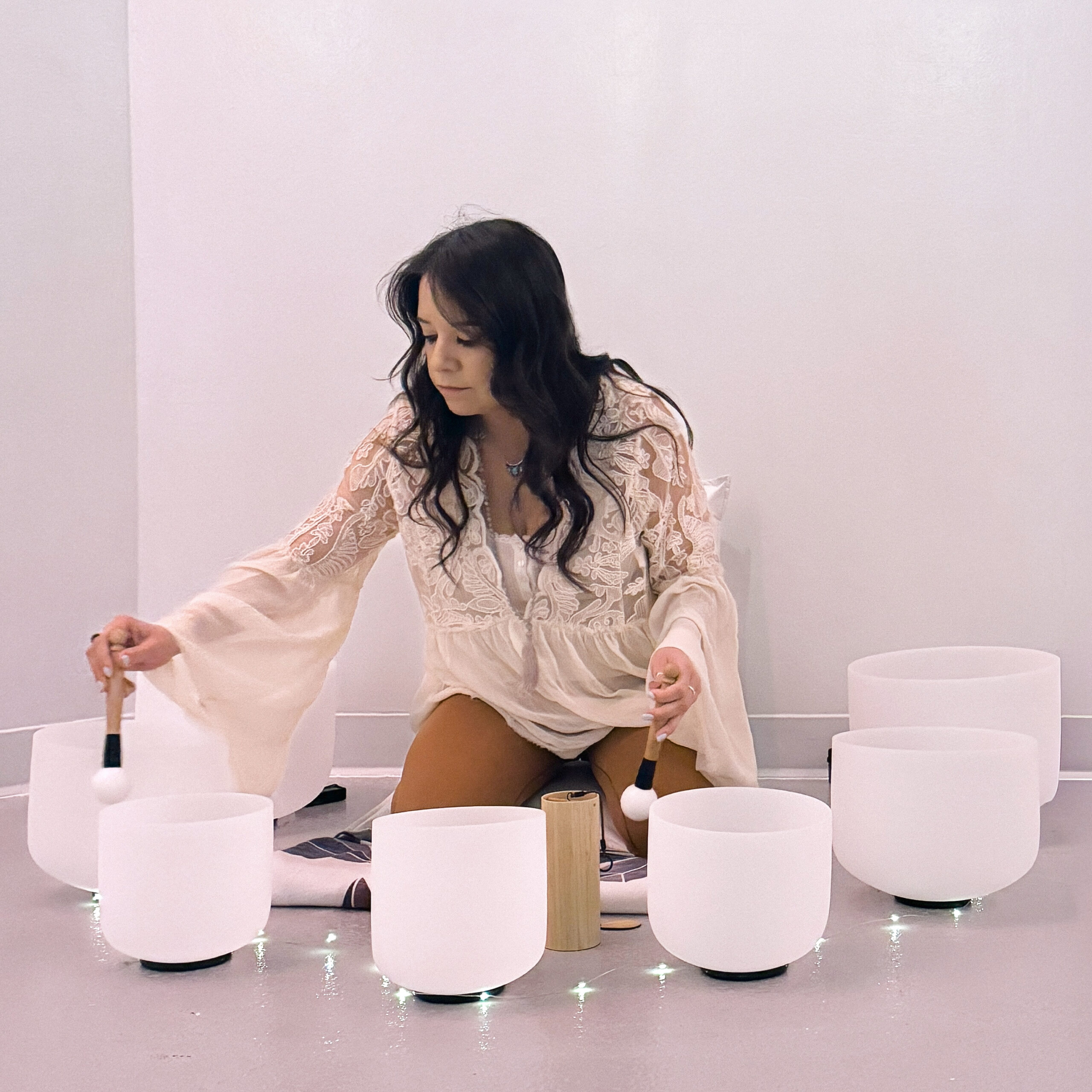 Woman playing crystal singing bowls during a soft-lit sound bath experience in a calm, minimal space