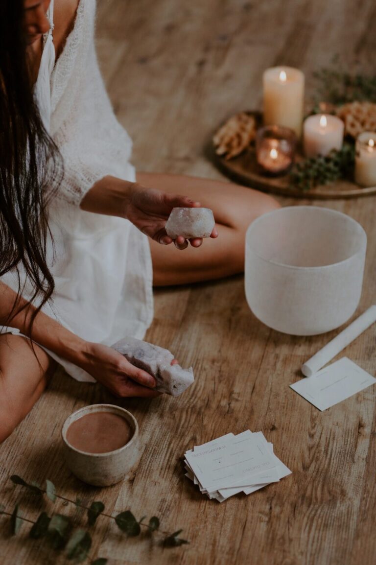 close up of woman holding crystals with cacao cup and crystal singing bowl on wooden floor