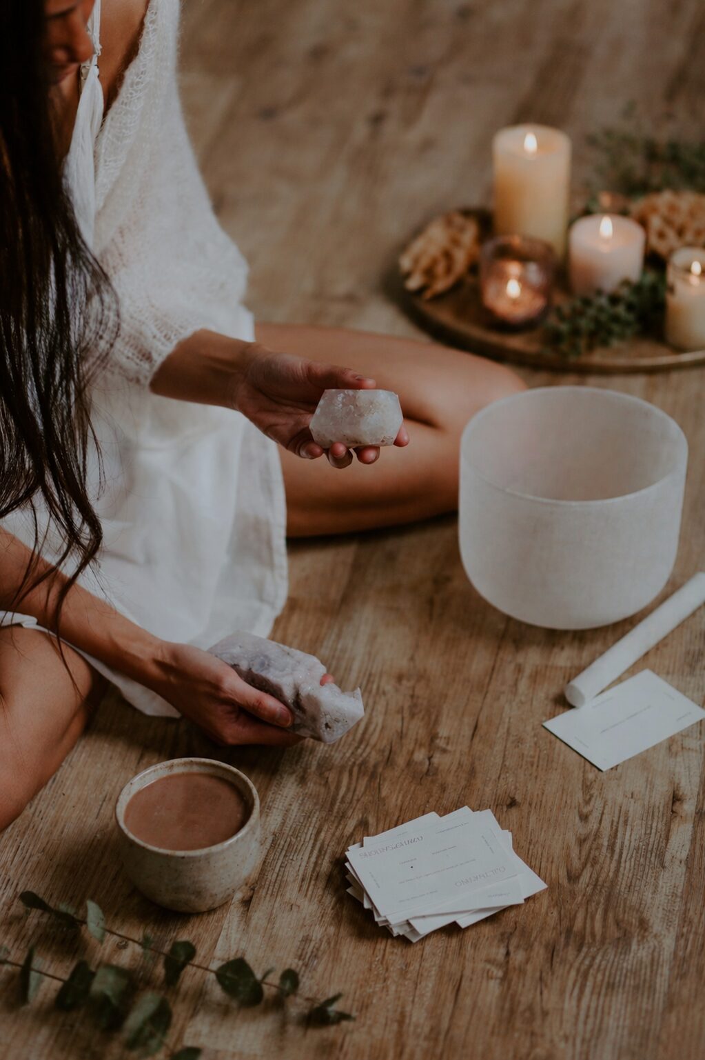 close up of woman holding crystals with cacao cup and crystal singing bowl on wooden floor