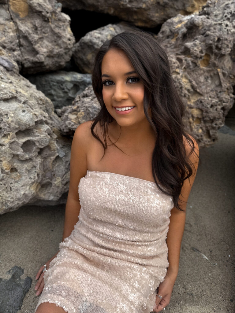 Kayla sitting by rocks wearing a neutral sequin dress smiling