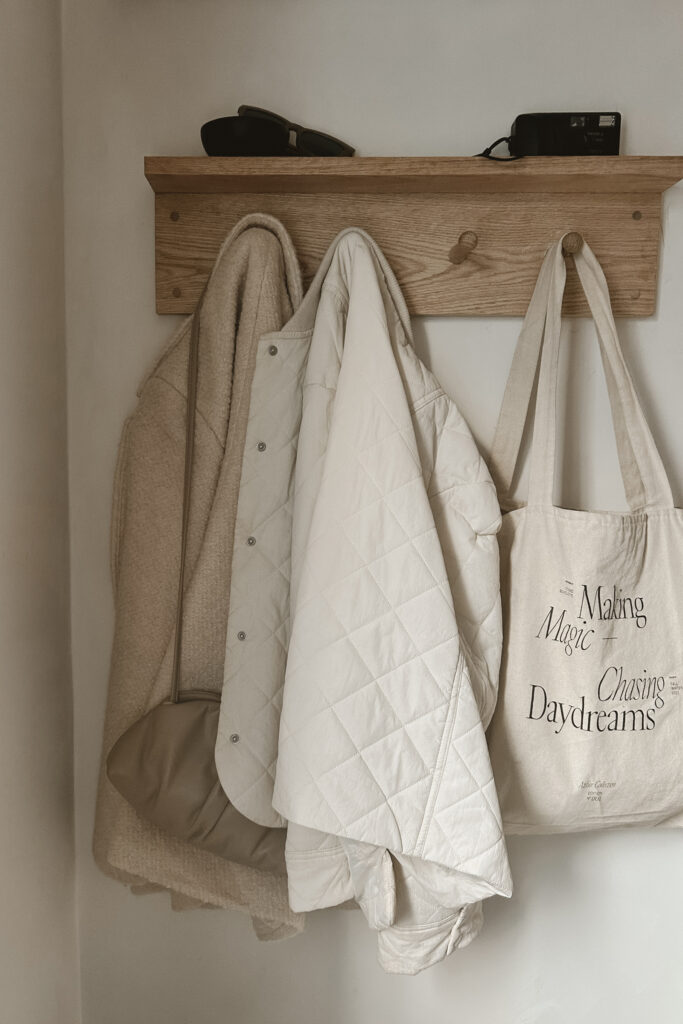 Neutral entryway with timeless outerwear and tote bag arranged on a wooden coat rack.