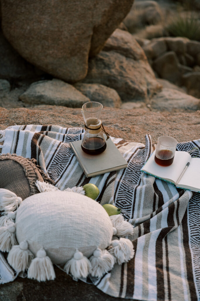 Cozy beach picnic with coffee, journals, blankets, and simple comforts during golden hour.