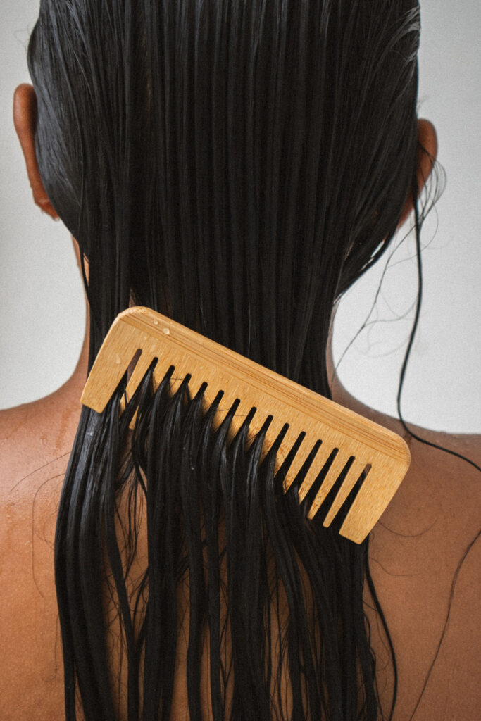 Wide-tooth bamboo comb gently detangling wet hair as part of an intentional everyday hair care routine.