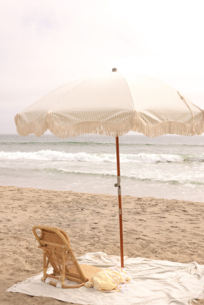 Vintage striped beach umbrella with a woven chair and blanket overlooking the ocean on a peaceful sandy beach.