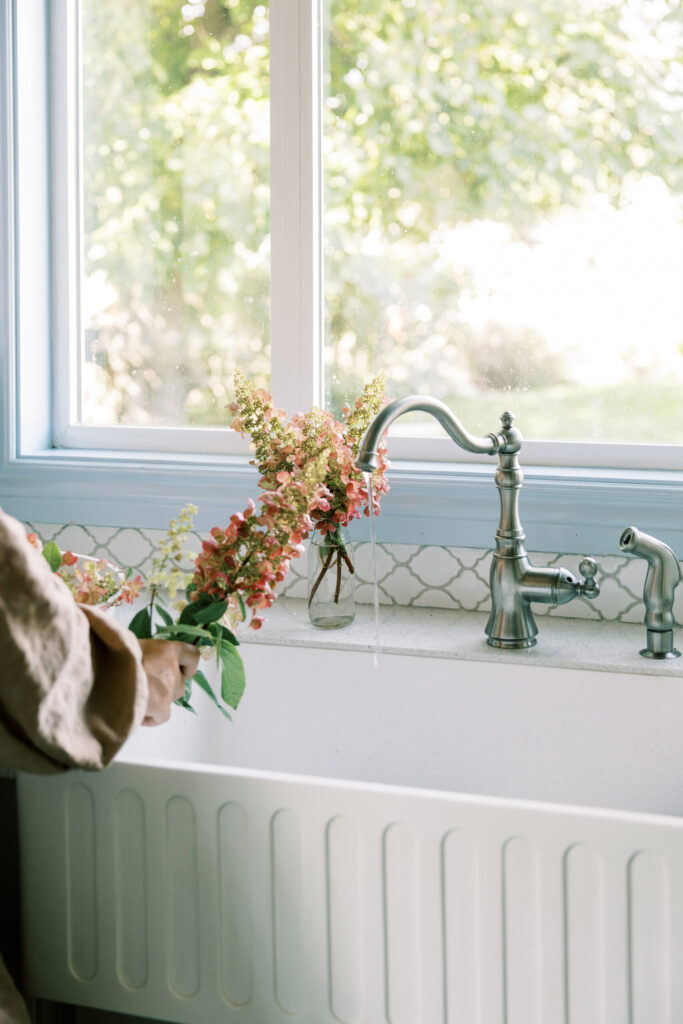 Fresh flowers in a vase beside a bright kitchen sink window