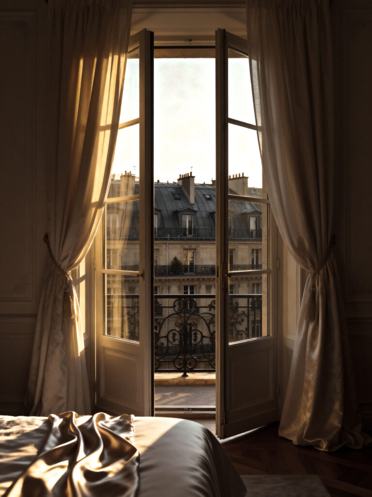 Sunlight streaming through open French windows in a Paris apartment bedroom